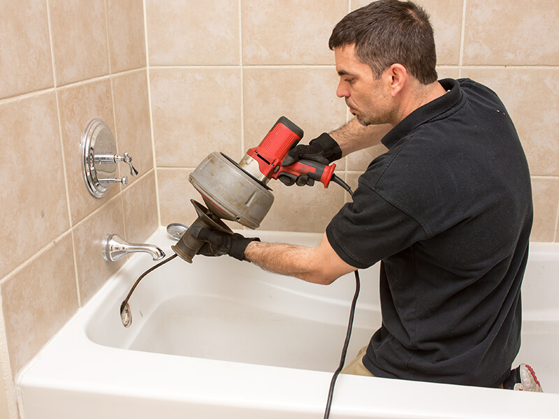 Plumber unclogging a tub drain with an electric auger.